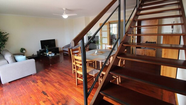 Una sala de estar moderna con una escalera de madera, un televisor de pantalla plana, una mesa de comedor con sillas y un sofá.