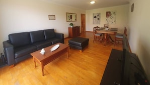 A living room with a black sofa, wooden coffee table, and a dining area with a wooden table and chairs. - Aqua Vista Lido Apartment by IZI Holiday Rentals, Aqua Vista Lido Apartment (Funchal)
