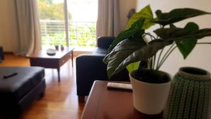 A living room with a sofa, a coffee table, a potted plant, and a view of the outdoors through a window. - Aqua Vista Lido Apartment by IZI Holiday Rentals, Aqua Vista Lido Apartment (Funchal)