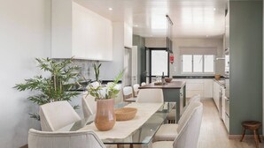 A modern kitchen with white cabinets, a dining area with a glass table, and a view of the adjacent living space. - Paul's Holiday House, Paul's Holiday House (Ponta Do Pargo)