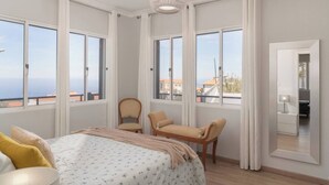 A bedroom with a bed, two chairs, a desk, and a large window offering a view of the sea. - Paul's Holiday House, Paul's Holiday House (Ponta Do Pargo)