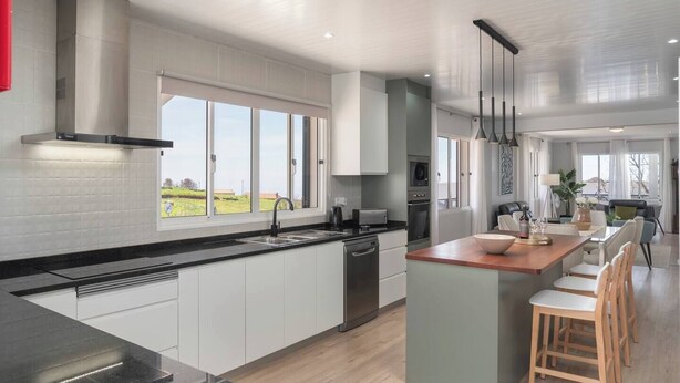 A modern kitchen with white cabinets, a black countertop, and a wooden island with bar stools. - Paul's Holiday House, Paul's Holiday House (Ponta Do Pargo)