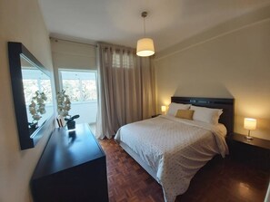Une chambre d’hôtel avec un lit, des lampes de chevet, une table de chevet, un miroir et une fenêtre avec des rideaux.