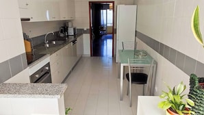 A compact kitchen with white cabinets, a granite countertop, and a dining area with a glass table and chairs. - Jardim Sol Holiday Apartment, Jardim Sol Holiday Apartment (Funchal)