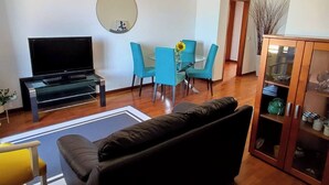 A living room with a flat-screen TV, a sofa, a dining table with chairs, a mirror, and a cabinet with glass doors. - Jardim Sol Holiday Apartment, Jardim Sol Holiday Apartment (Funchal)