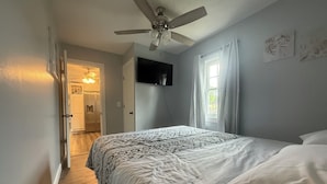 A bedroom with a bed, a ceiling fan, a TV mounted on the wall, and a window with curtains. - Corner Cottage 2 bedroom pets welcome and close to downtown (Ashland)