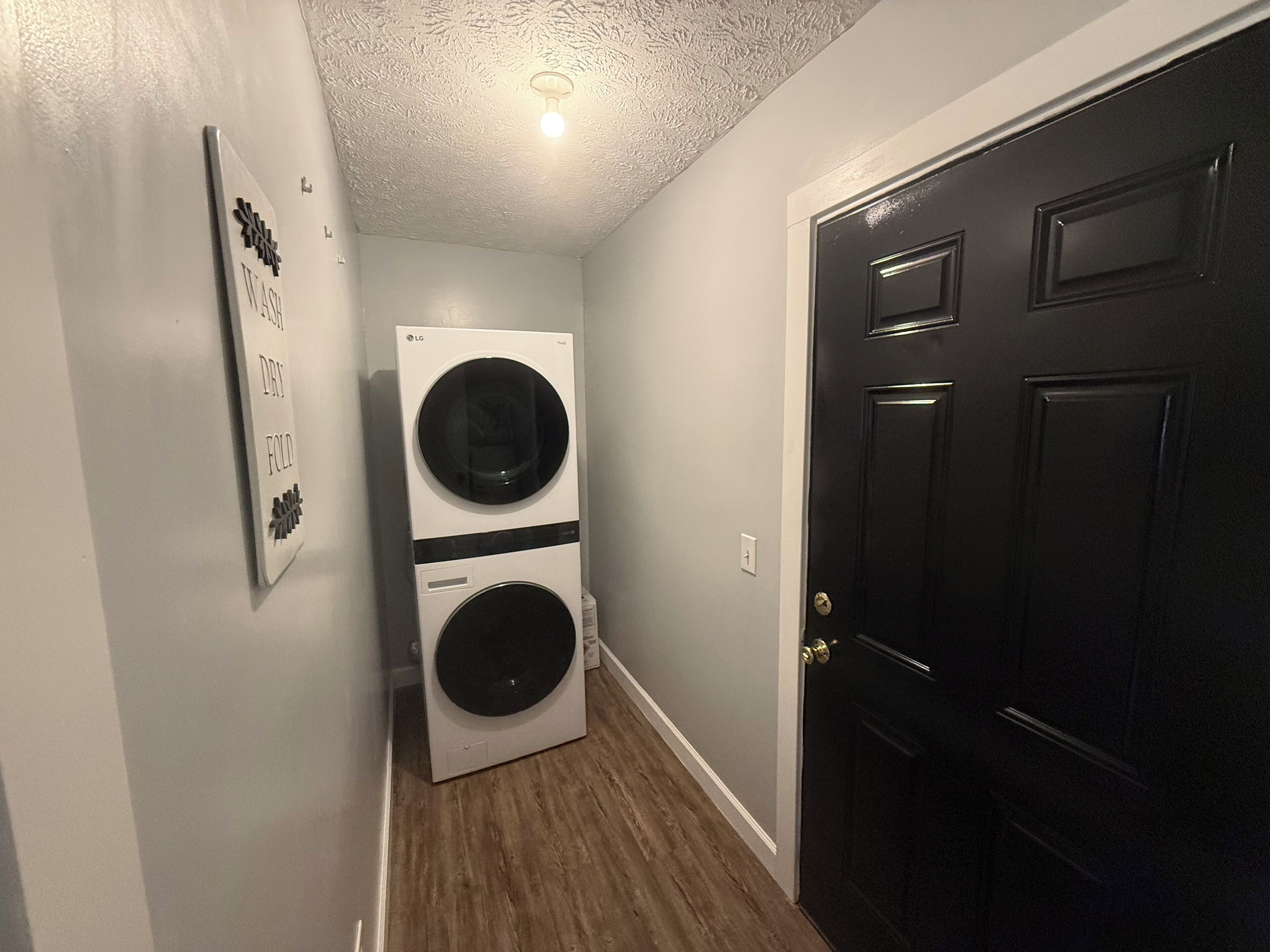 A laundry room with a stacked washer and dryer, a door, and a wall-mounted sign.