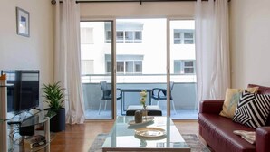A living room with a glass coffee table, a red sofa, a TV, and a balcony with chairs.
