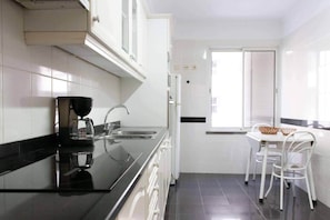 A modern kitchen with a black countertop, stainless steel appliances, and a dining area with white chairs and a table. - Elsa's Place, Elsa's Place . (Funchal)