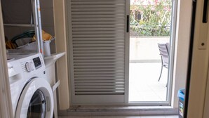 A laundry area with a washing machine and dryer, a sliding door to a balcony, and a trash bin.