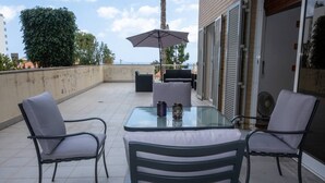 An outdoor patio with a glass table, two chairs, an umbrella, and a grill.