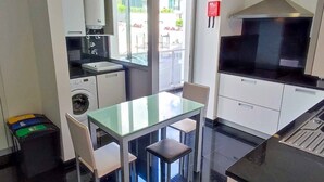 Una cocina compacta con zona de comedor, lavadora y un amplio ventanal con vistas al exterior.