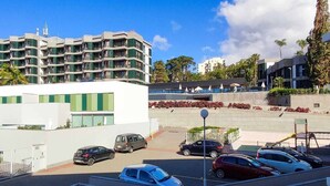 Un estacionamiento con varios autos, un edificio moderno con balcones y un área ajardinada con plantas y un muro.