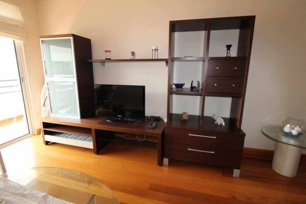 A living room with a wooden entertainment unit, a television, and a glass coffee table.