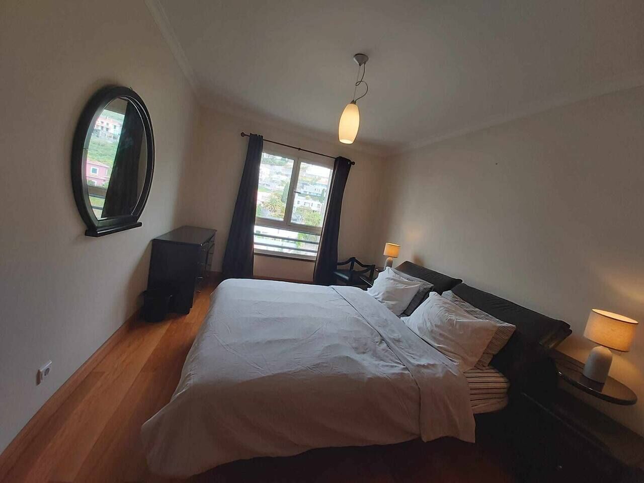 Ein Schlafzimmer mit Bett, Nachttischen, einem Spiegel und einem Fenster mit Vorhängen.