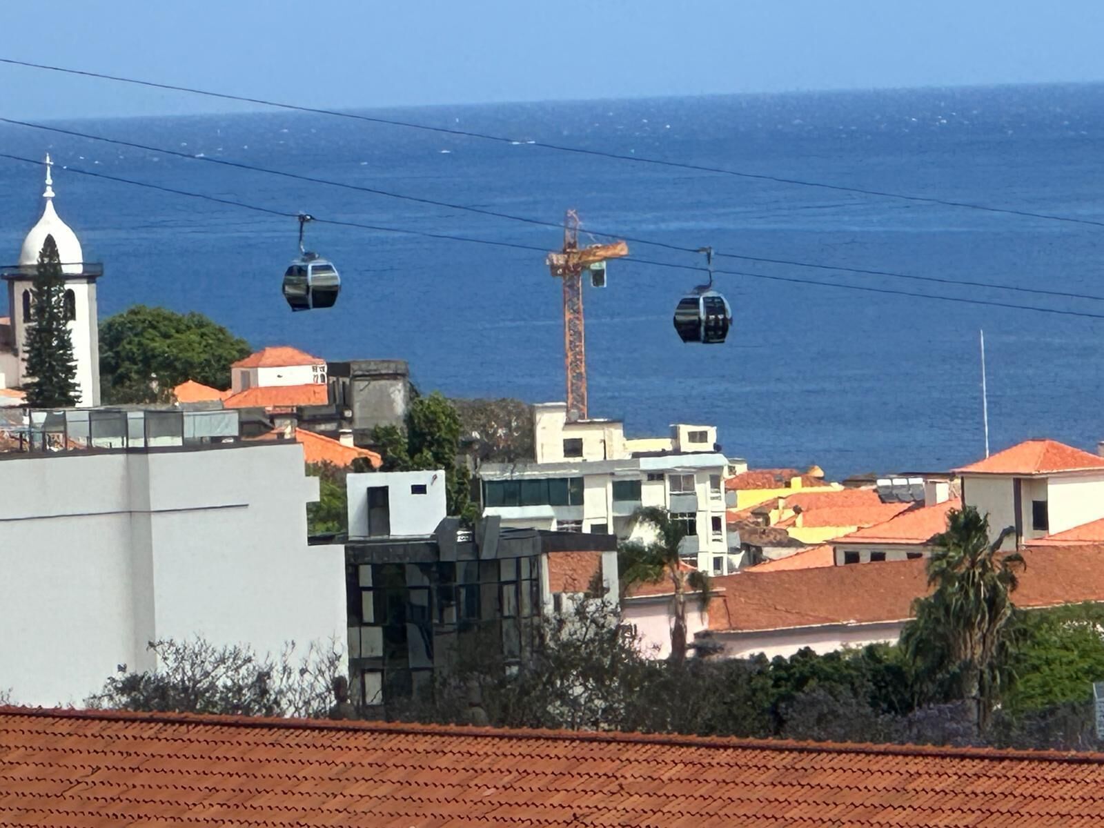 Une ville côtière dotée d’un téléphérique, de bâtiments aux toits recouverts de tuiles rouges et d’un clocher d’église.