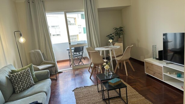 A modern living room with a sofa, a coffee table, a TV, and a dining area with chairs and a table.