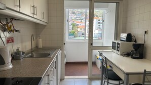 A compact kitchen with white cabinets, a sink, a stove, and a window overlooking a residential area.