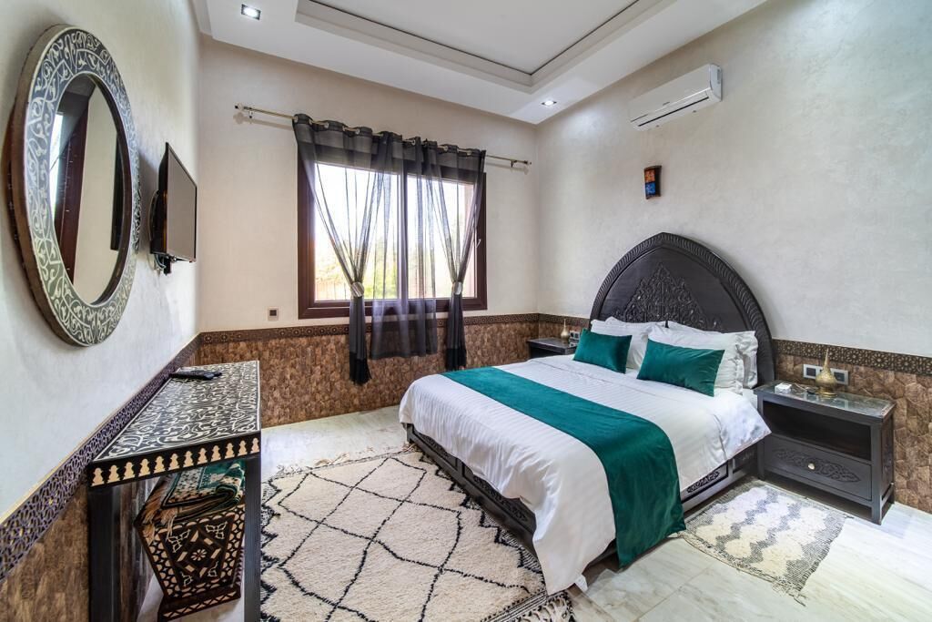 Un dormitorio con una cama grande, televisión, ventana con cortinas y una alfombra estampada.