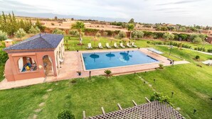 A pool area with lounge chairs, a small building with arches, and a view of the surrounding landscape. - Luxury stay near Marrakech with mountain views, pool, and family fun (Marrakesh)