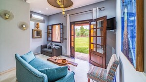 A living room with a sofa, a coffee table, and a patterned chair. There is a television on the wall and a painting above it. - Luxury stay near Marrakech with mountain views, pool, and family fun (Marrakesh)