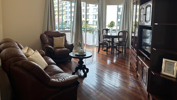 A living room with a leather sofa, a dining table with chairs, a chandelier, and a large black cabinet. - Robert Apartment in Ajuda (Funchal)
