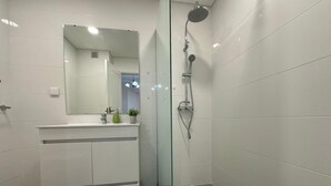 A modern bathroom with a glass shower enclosure, a white vanity with a mirror, and a small potted plant. - Robert Apartment in Ajuda (Funchal)