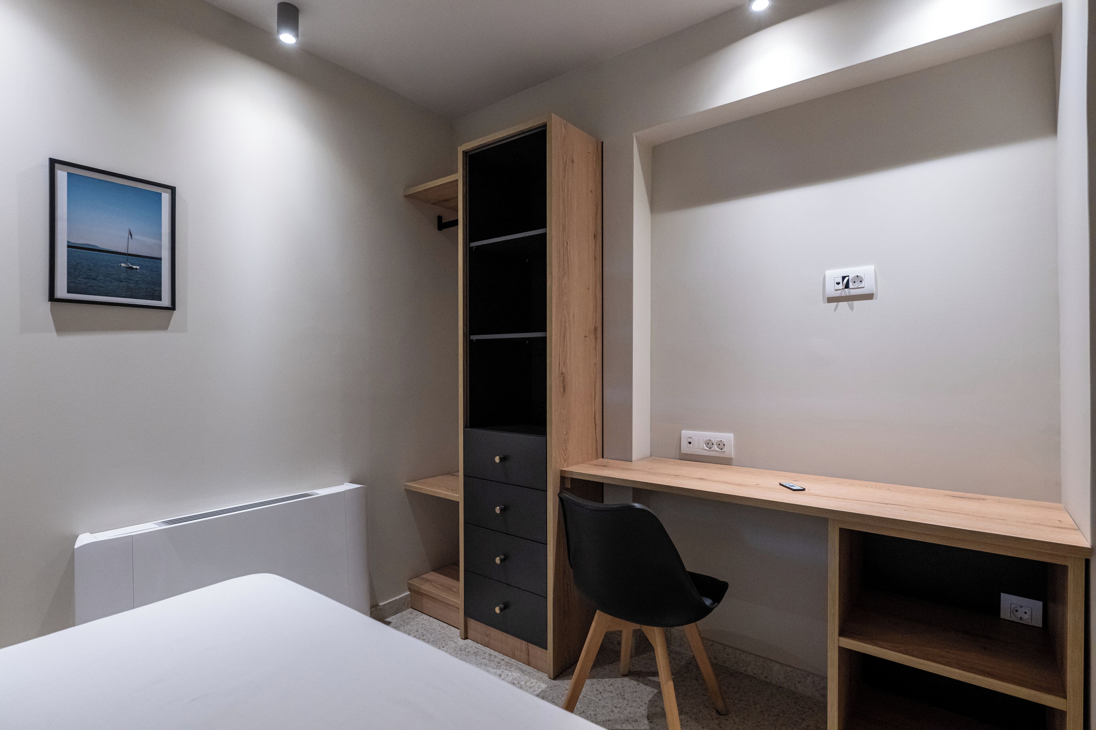 A bedroom with a bed, a desk, a chair, a wardrobe, and a picture on the wall.