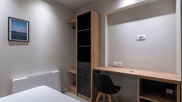 A bedroom with a bed, a desk, a chair, a wardrobe, and a picture on the wall.