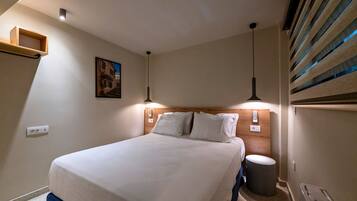 Een hotelkamer met een bed, nachtlampjes, een klein prullenbakje en een wandplank.