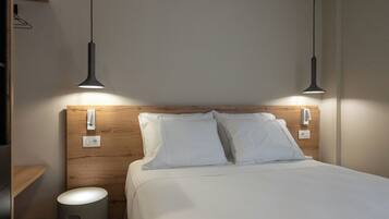 A neatly made bed with white linens, a wooden headboard, and two pendant lights.