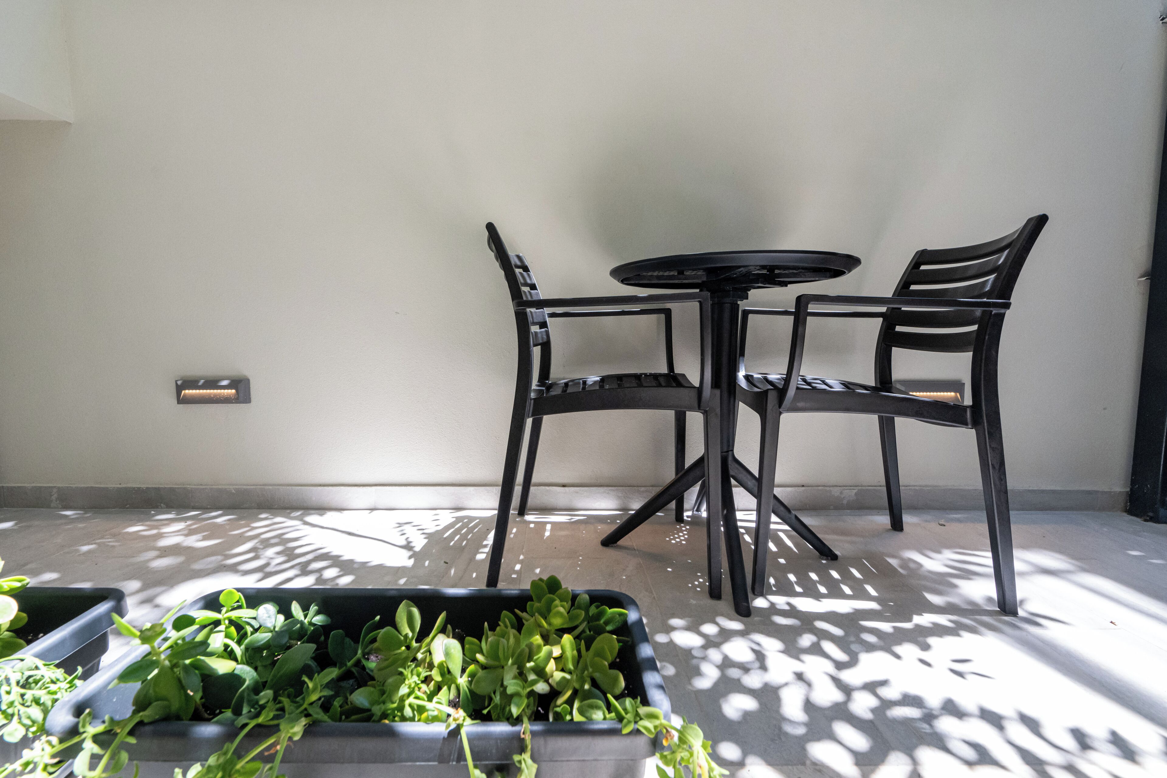 A small patio area with a round table and two chairs, surrounded by potted plants.