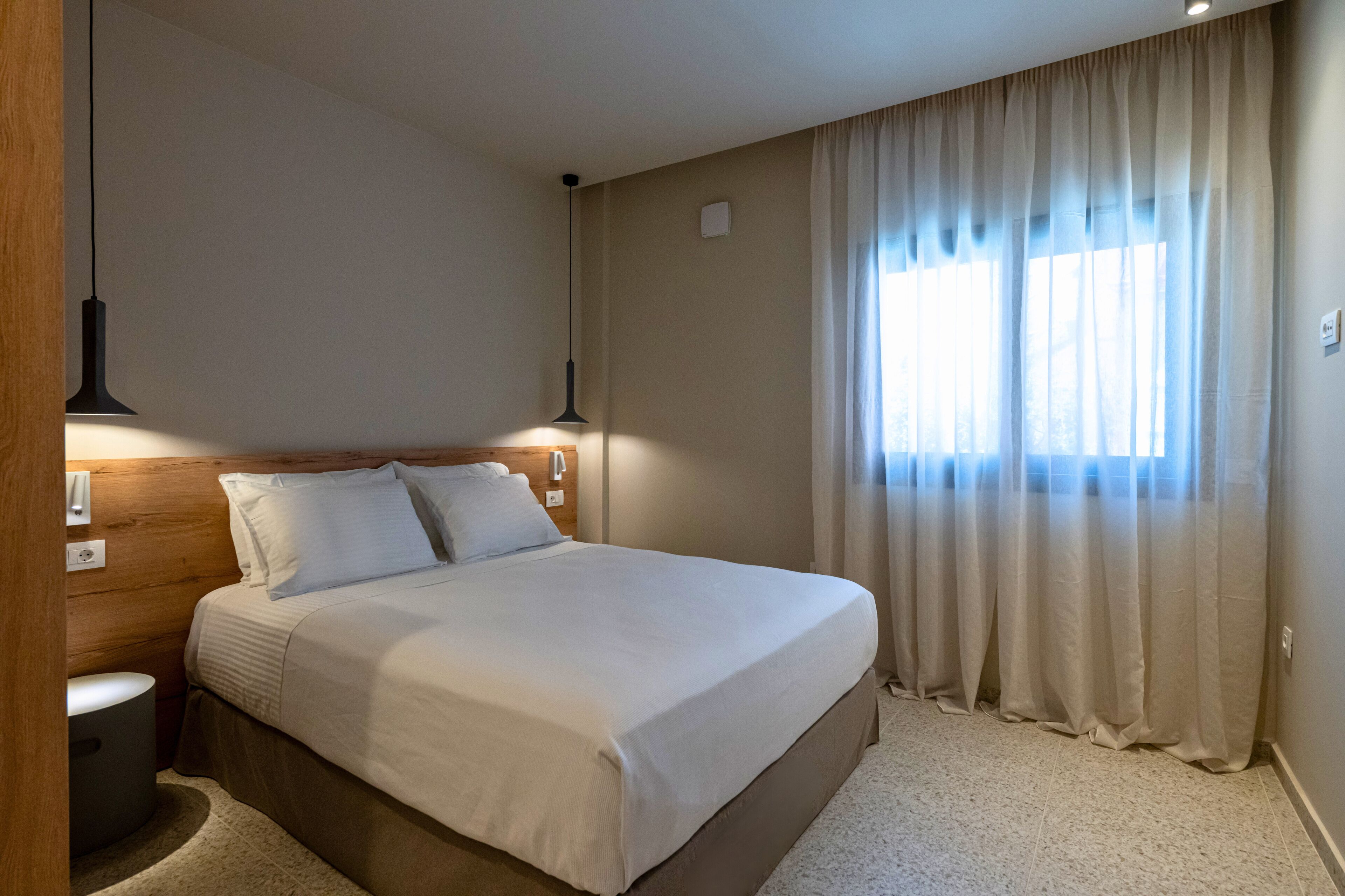 A neatly made bed with white linens, a wooden headboard, and two bedside lamps.