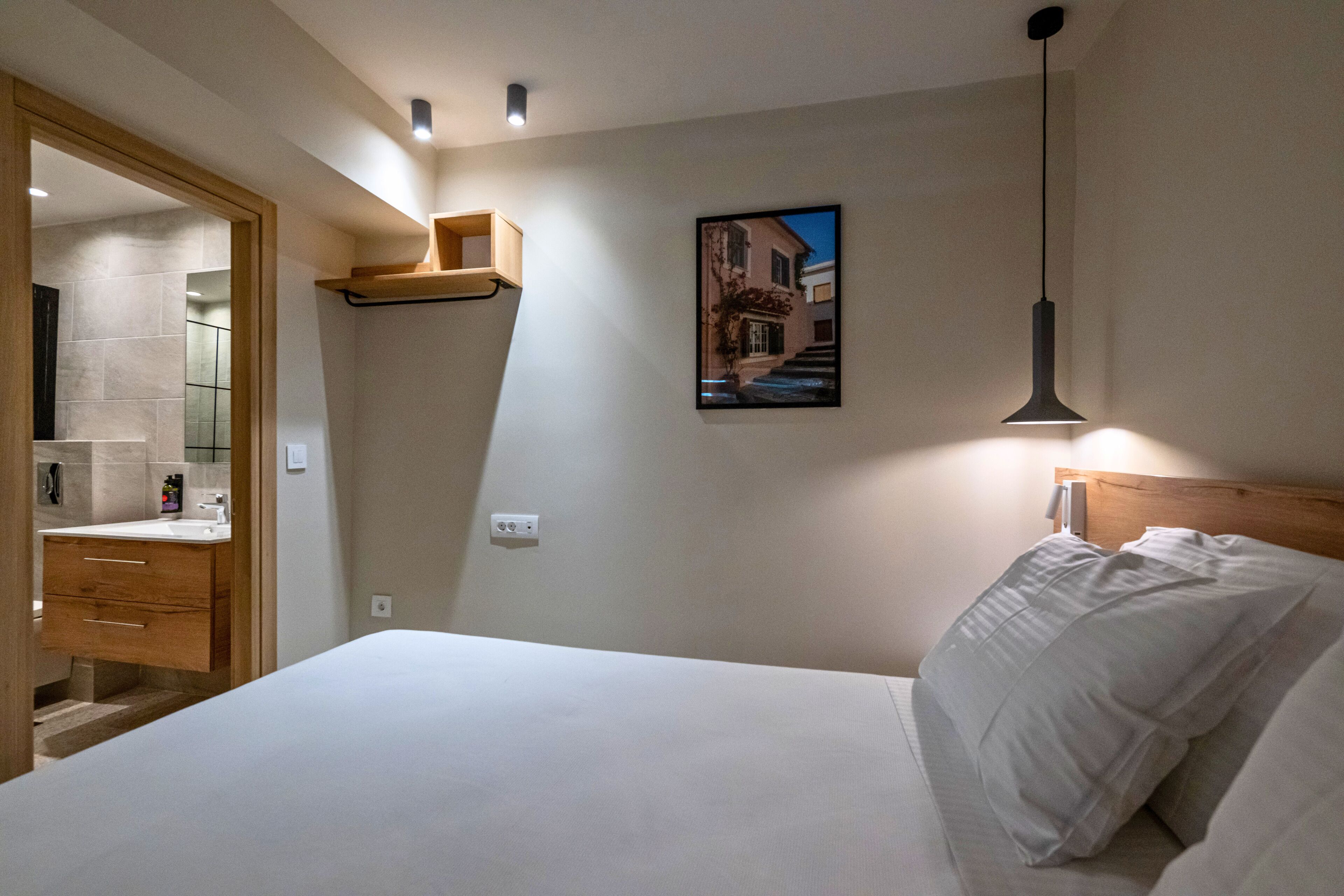 Une chambre à coucher avec un lit, une tête de lit en bois, une étagère fixée au mur, un tableau et une suspension lumineuse.