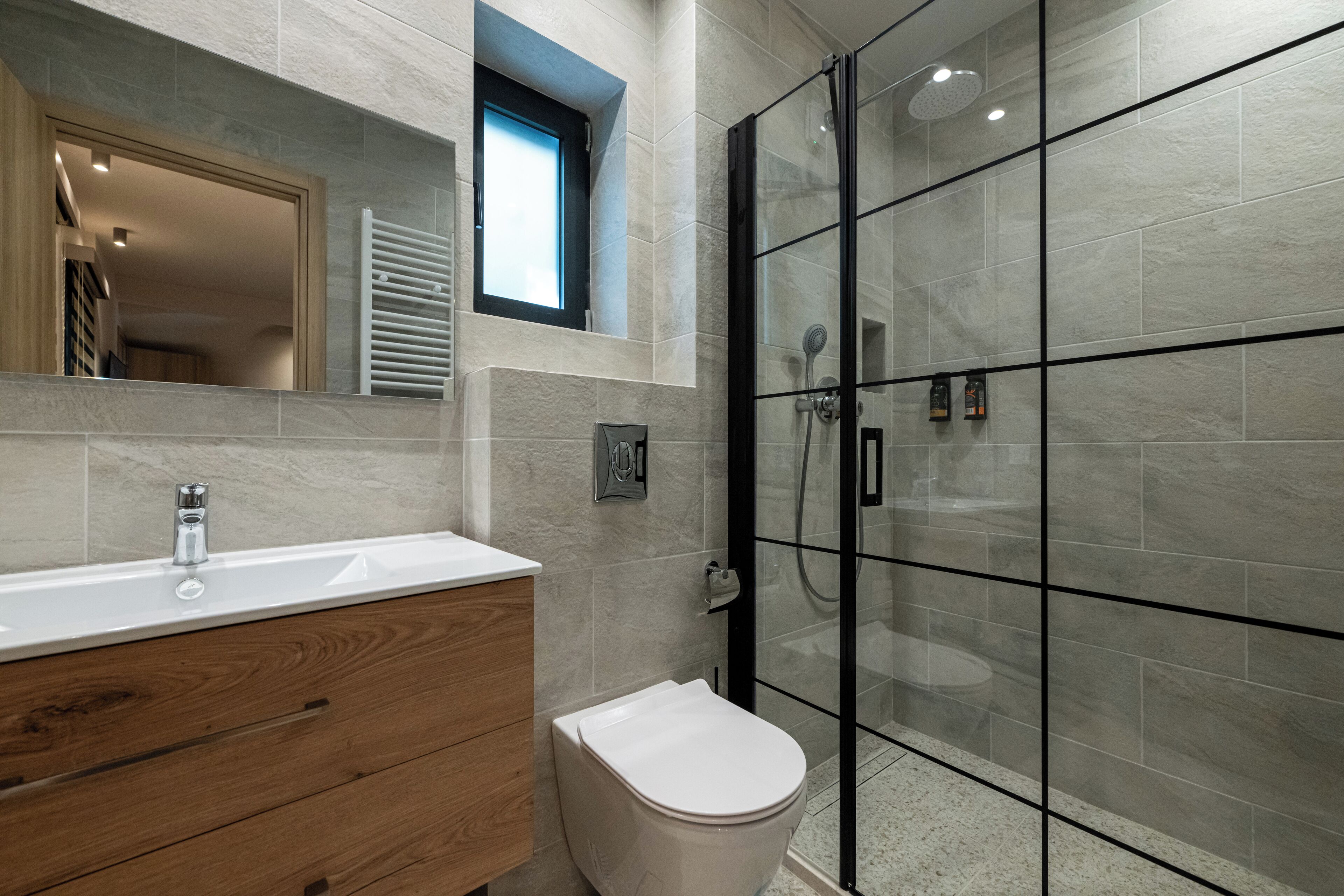 A modern bathroom with a glass shower enclosure, a wooden vanity, and a white toilet.
