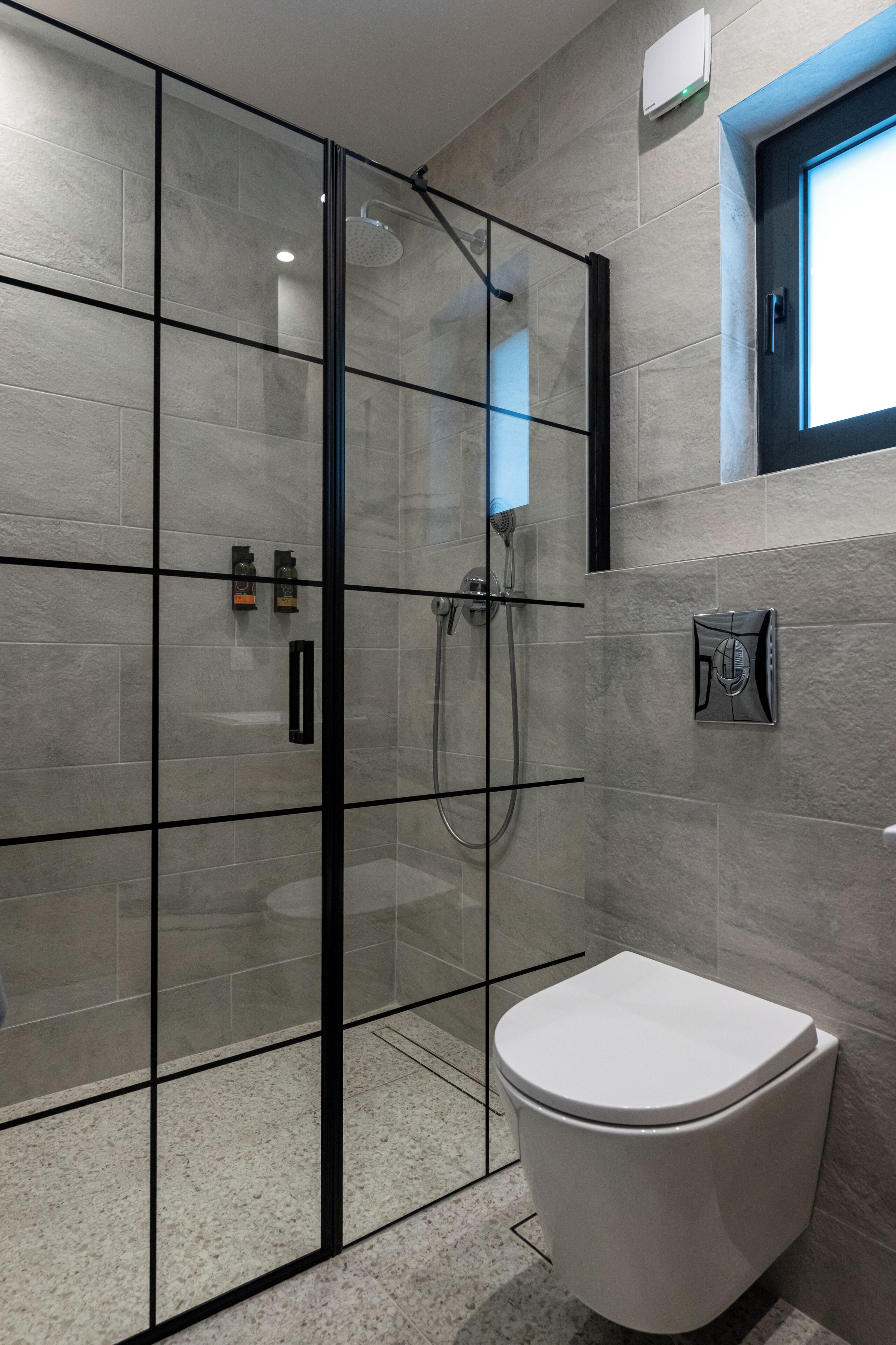 A modern bathroom with a glass shower enclosure, a white toilet, and a wall-mounted heater.