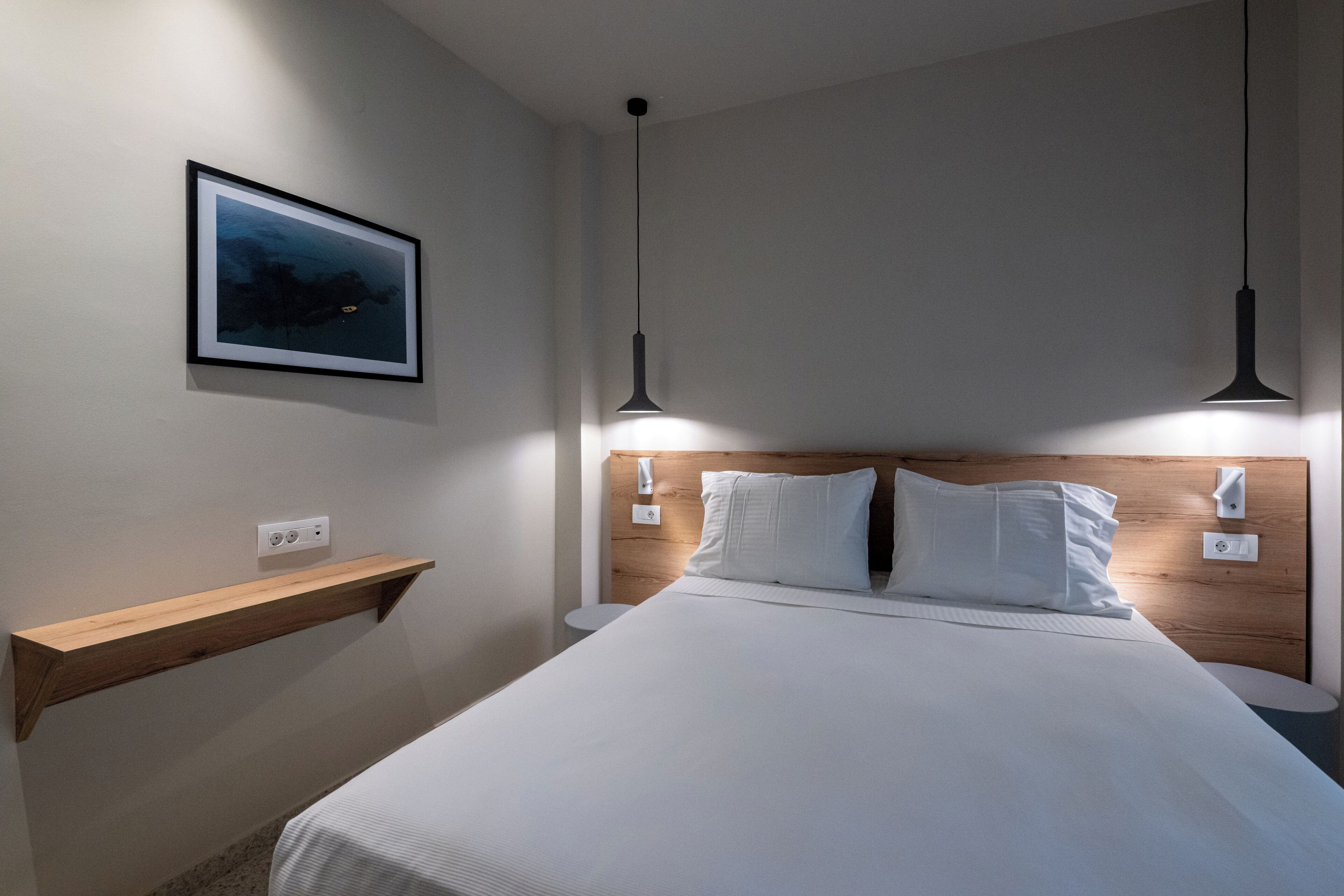 A neatly arranged hotel room with a bed, bedside tables, a framed picture on the wall, and pendant lighting.