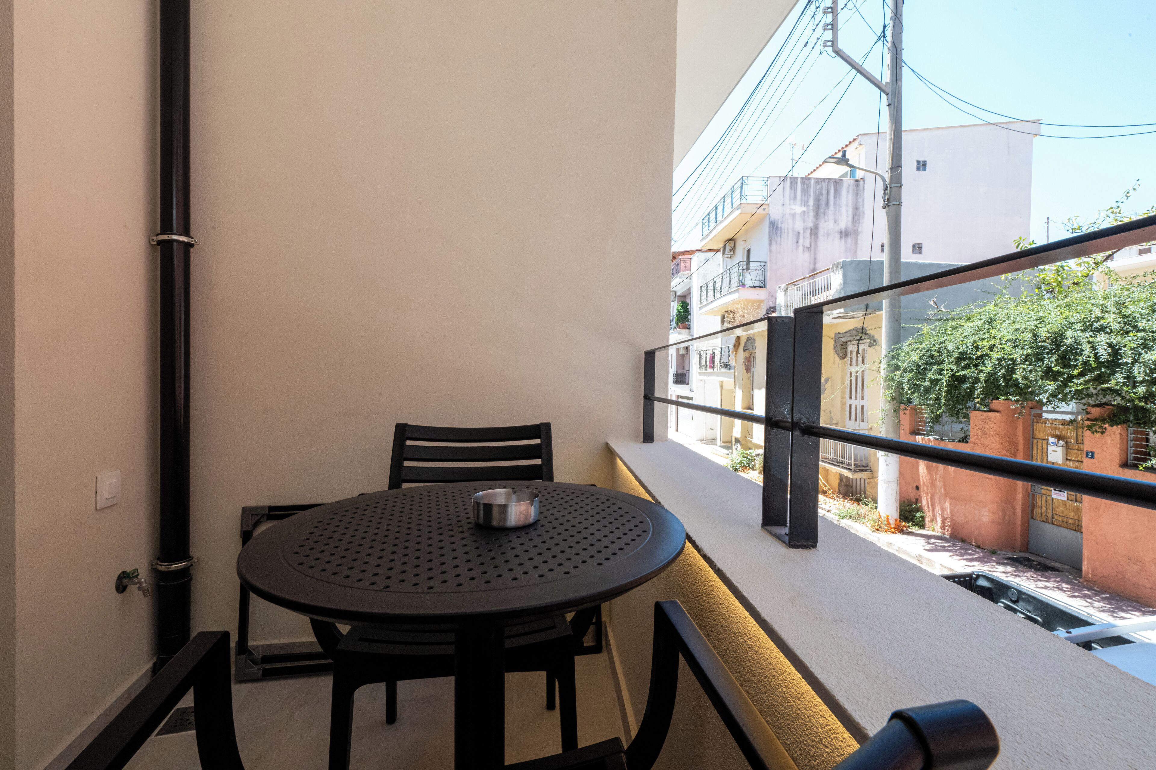 A balcony with a round table and chairs, a metal bowl, and a view of buildings and a tree.