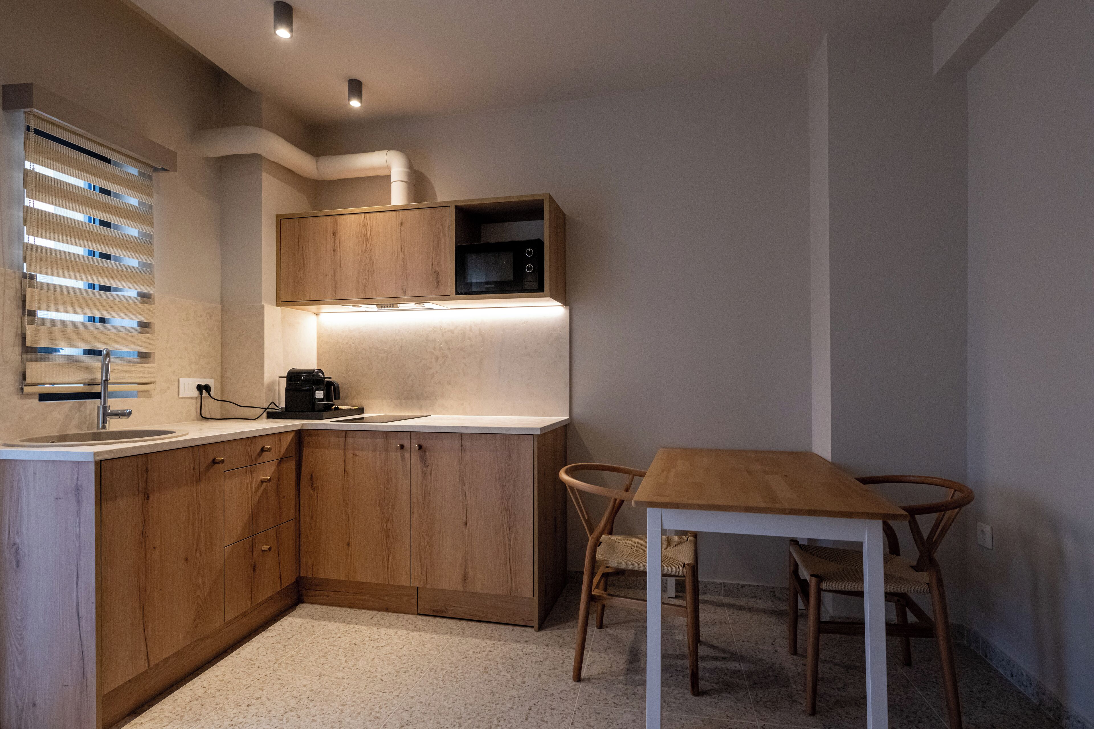 A compact kitchen with wooden cabinets, a microwave, a coffee machine, and a dining area with a table and chairs.