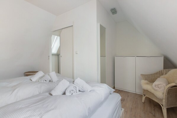 Ein Schlafzimmer mit zwei Betten, einem Korbsessel und einem Kleiderschrank.