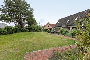 A residential property with a well-maintained lawn, a brick pathway, and a large tree.