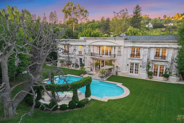 A large, two-story house with a swimming pool and a well-maintained lawn.