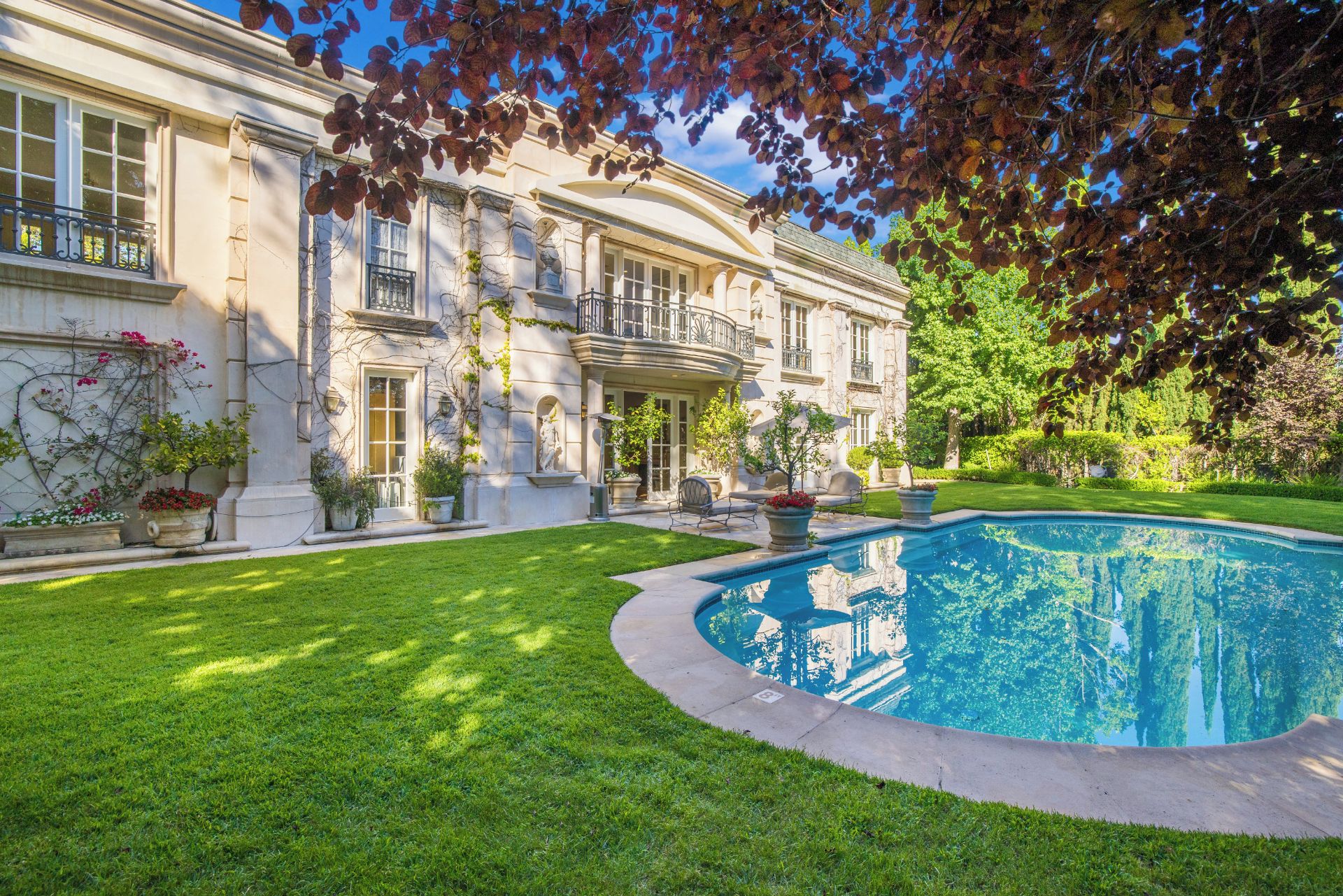 A large, classical building with a swimming pool, surrounded by well-maintained lawns and mature trees.