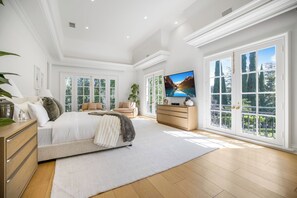 Een ruime slaapkamer met een groot bed, een dressoir, een televisie en uitzicht op een bergachtig landschap door grote ramen.
