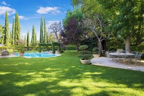 Un jardin bien entretenu, doté d’une piscine, d’une terrasse avec mobilier d’extérieur et de divers arbres.