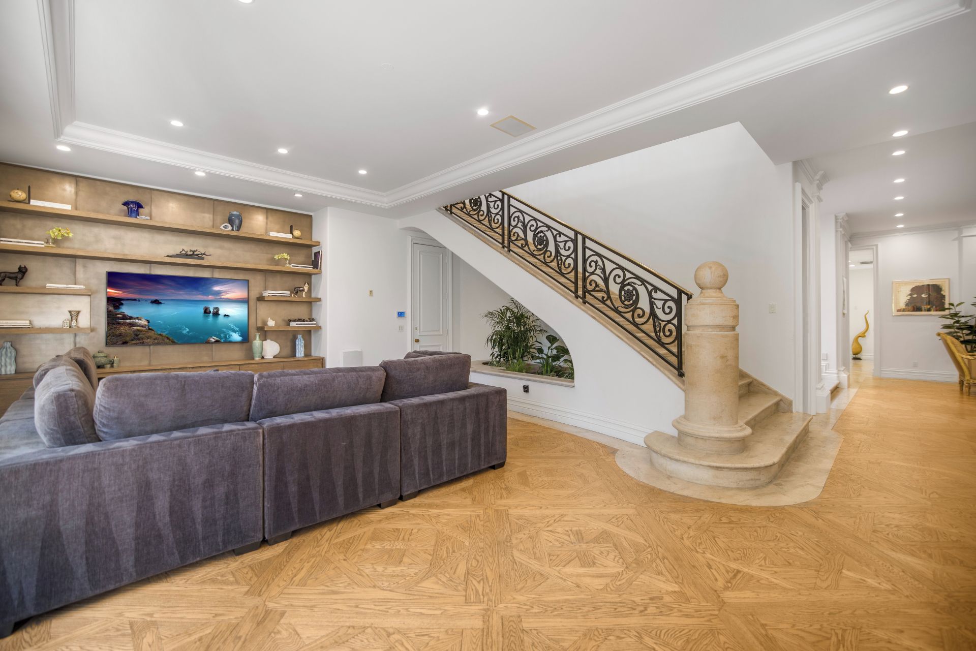 Ein großzügiges Wohnzimmer mit einer grauen Eckcouch, einem fest installierten Flachbildfernseher und einer Holztreppe mit einer dekorativen Geländer.