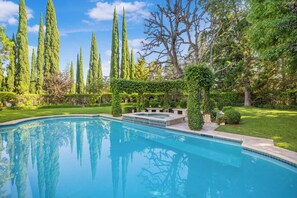 Une piscine entourée de grands arbres et bordée d’une pelouse bien entretenue.