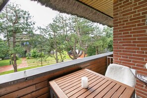 Un balcon avec une table en bois, une bougie blanche et une vue sur des arbres et un immeuble.