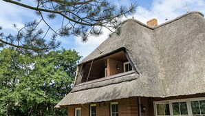 A traditional thatched-roof house with a brick base, large windows, and a balcony.