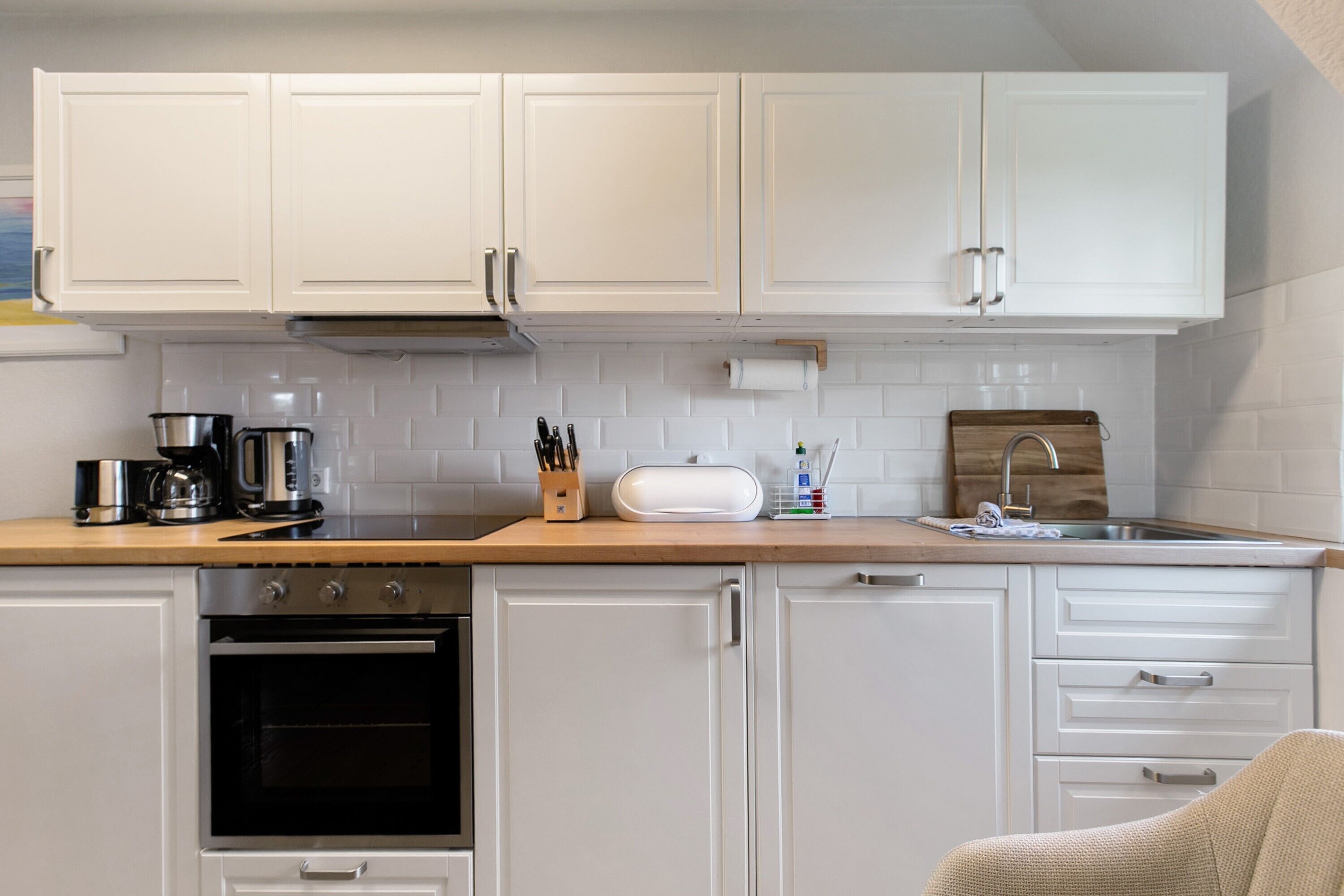 A kitchen with white cabinets, a wooden countertop, a coffee maker, a toaster, and a sink.